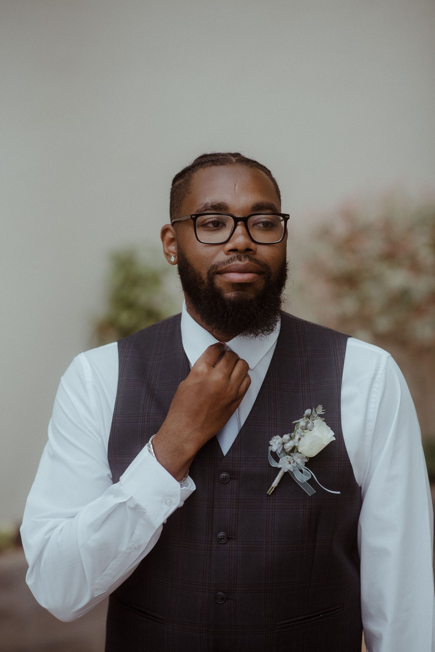 Groom adjusting tie while wearing vest and boutonniere.