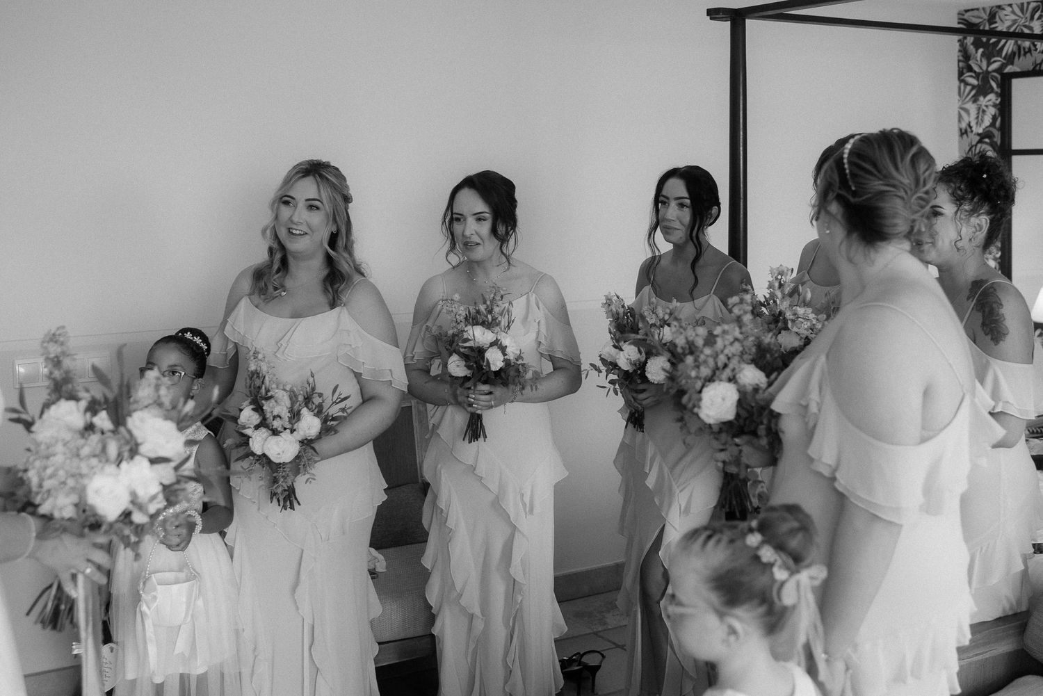 Black and white photo of bridal party in light colored dresses holding floral bouquets.