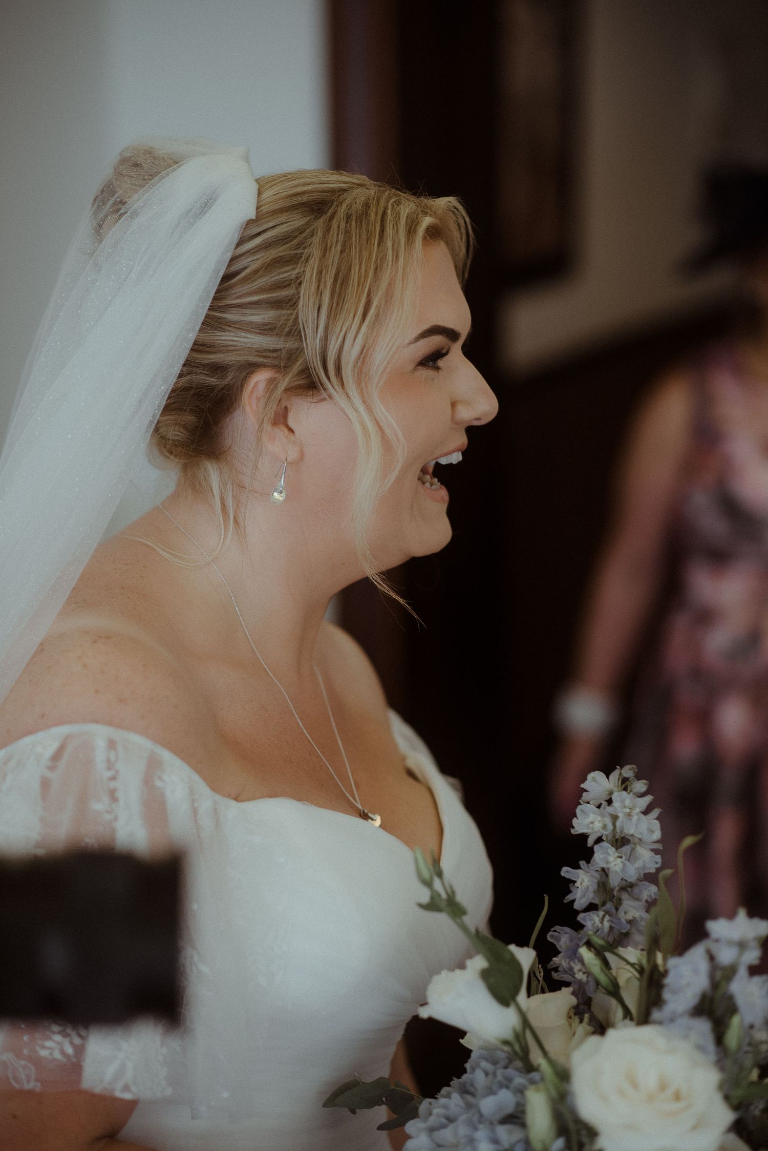 Side profile of a bride laughing while holding her wedding bouquet.