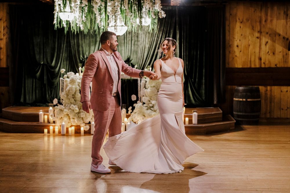 Couple dances together on wooden floor under hanging floral decor and candles at elegant wedding reception.