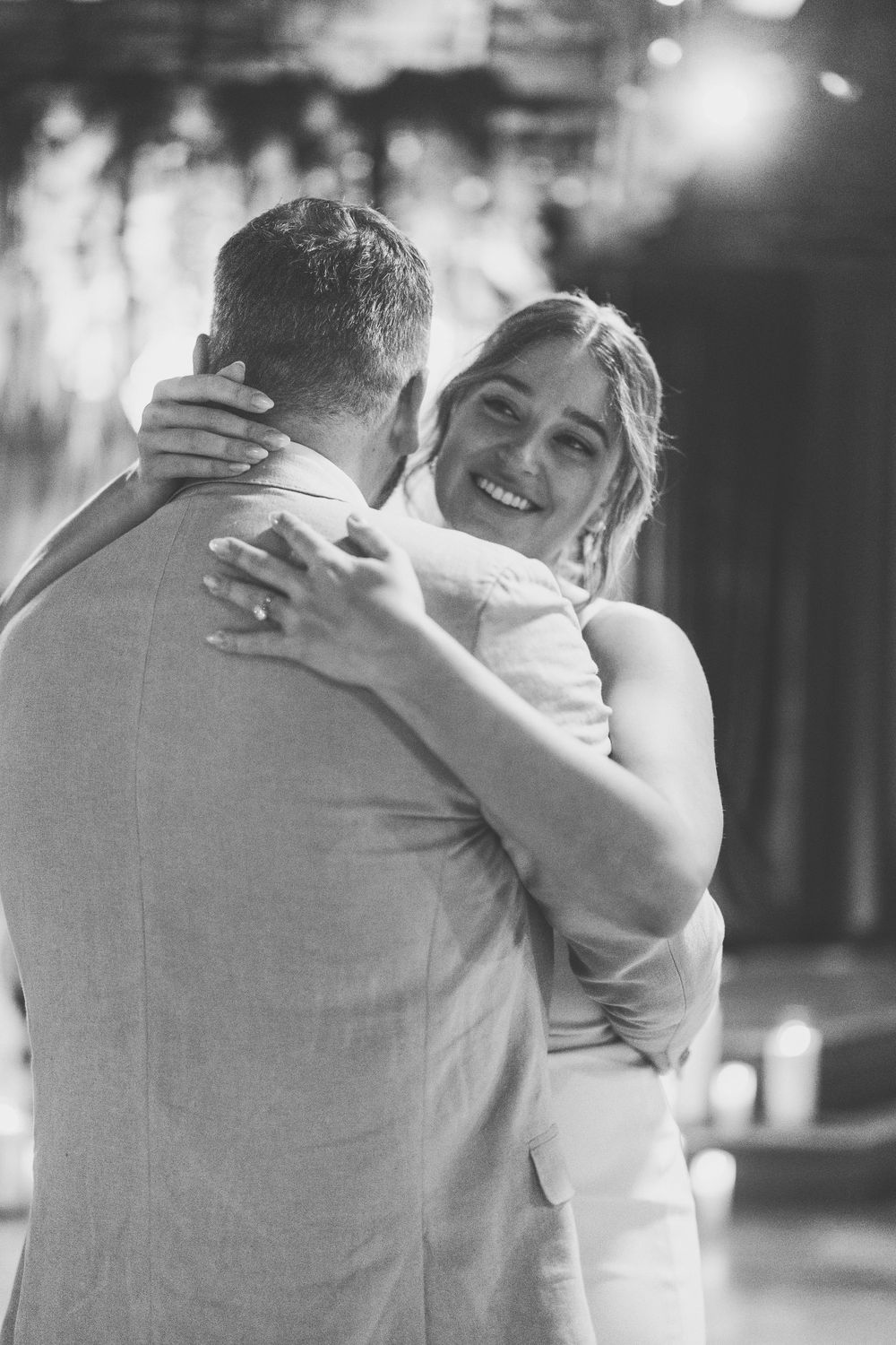 Black and white photo of newlyweds sharing their first dance, with the bride smiling joyfully during an intimate moment.