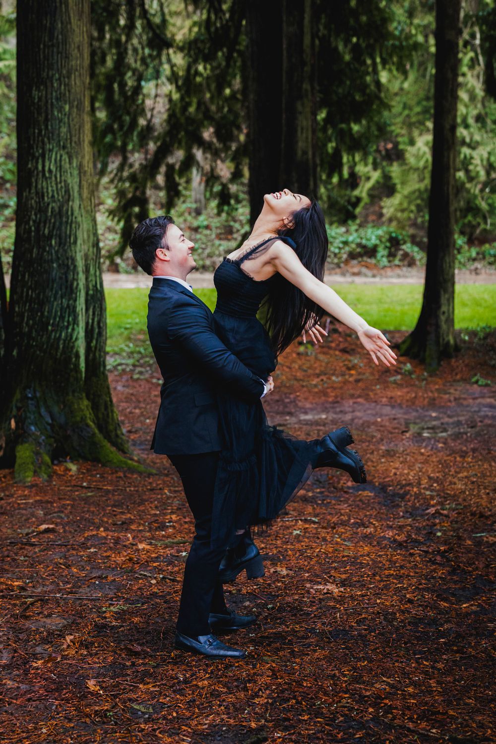 A joyful couple dancing playfully in a forest, with one person lifting the other in an energetic pose.