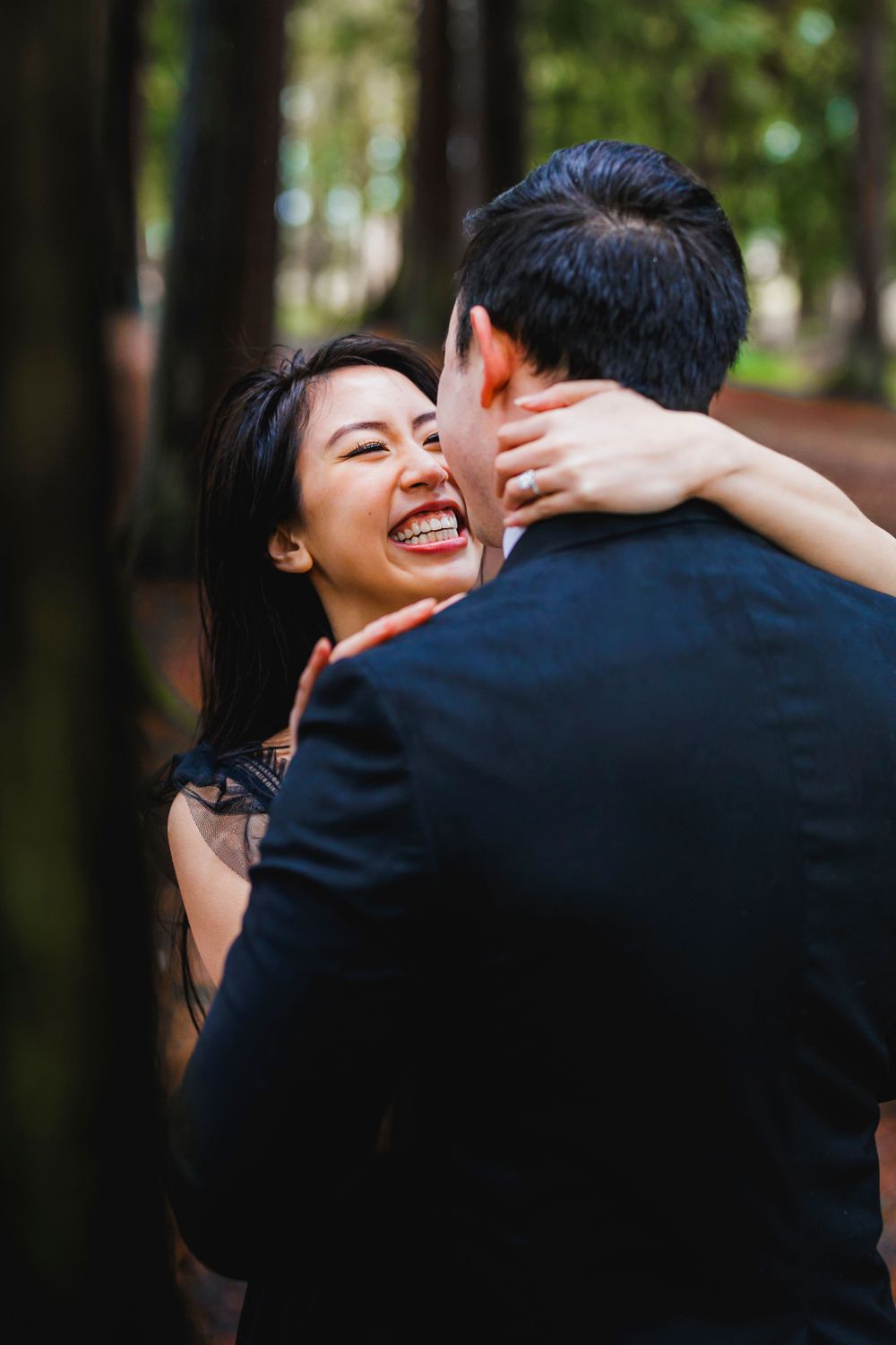 A couple sharing an intimate embrace and joyful laughter in a wooded outdoor setting.