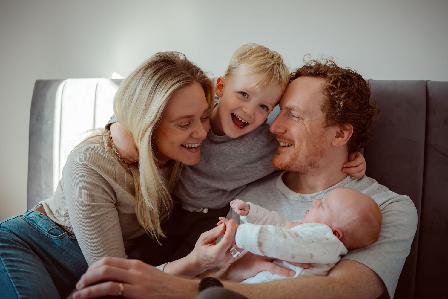Joyful family shares a tender moment together on a couch while holding newborn baby.