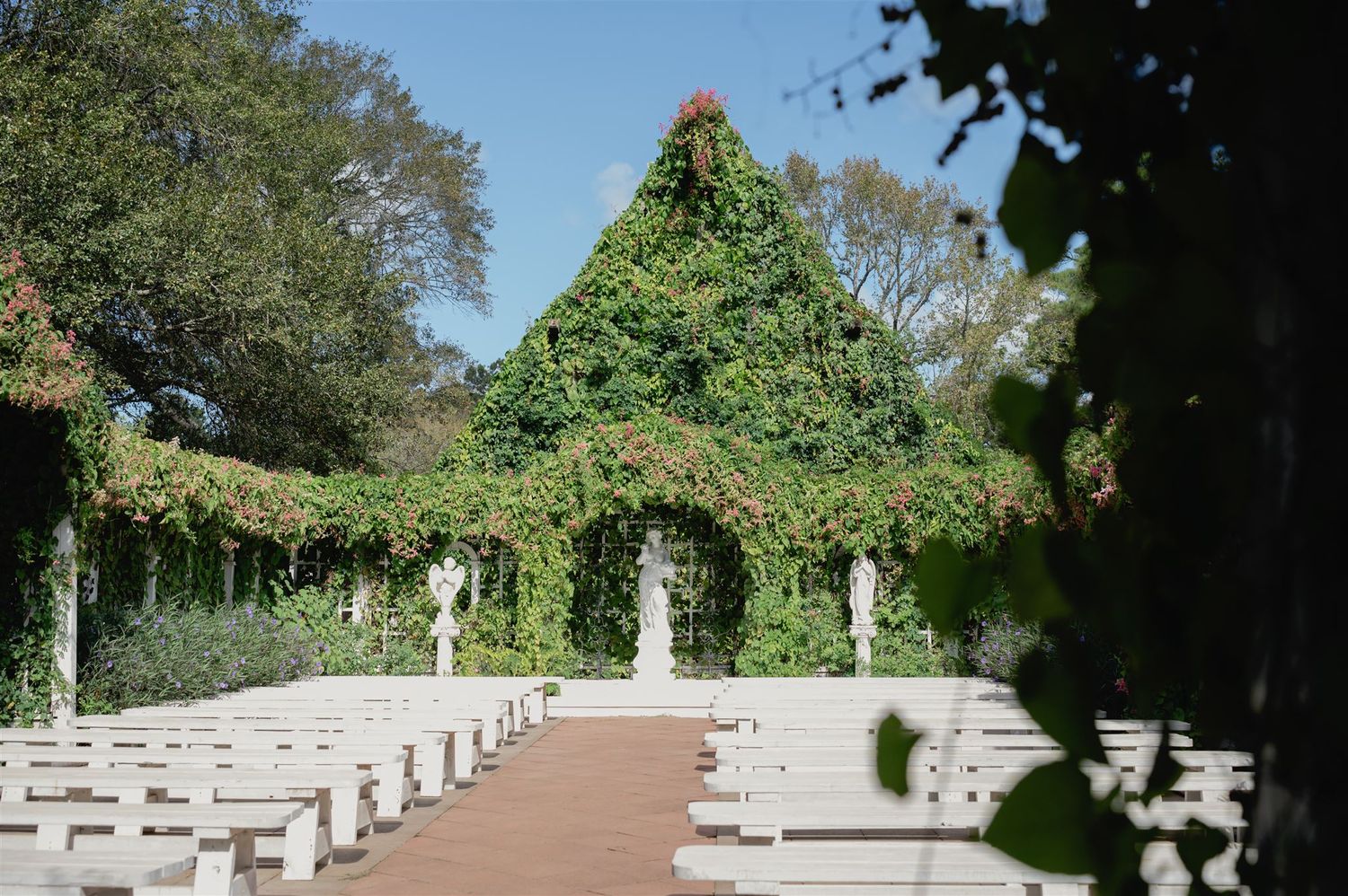 Outdoor wedding ceremony venue with white chairs and a grand ivy-covered arched structure at the end of the aisle.