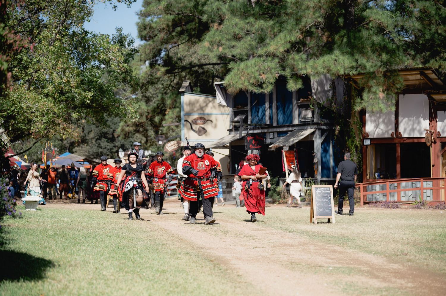 Traditional Japanese performers in red and white costumes gather outside historic shrine buildings during a cultural event.
