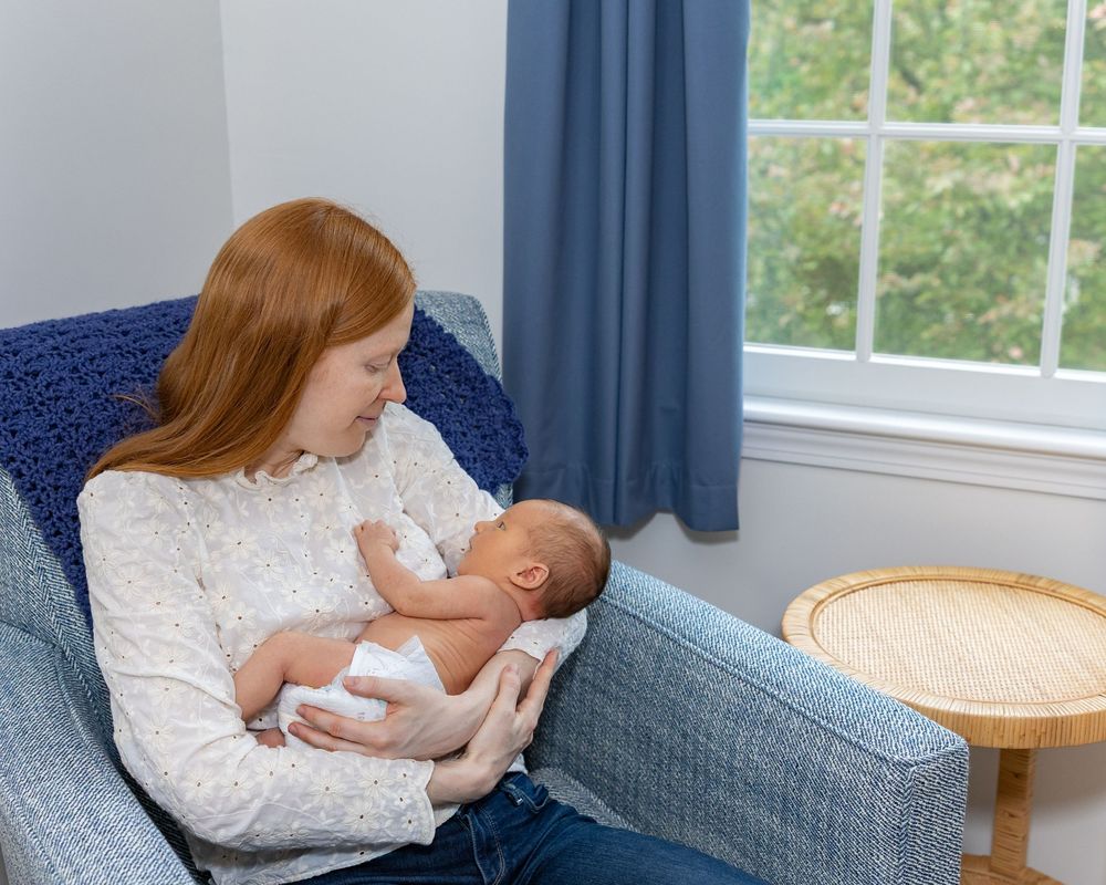Baby rests peacefully in a cozy armchair by a window during a newborn portrait photo shoot in Sudbury, MA outside Boston, MA
