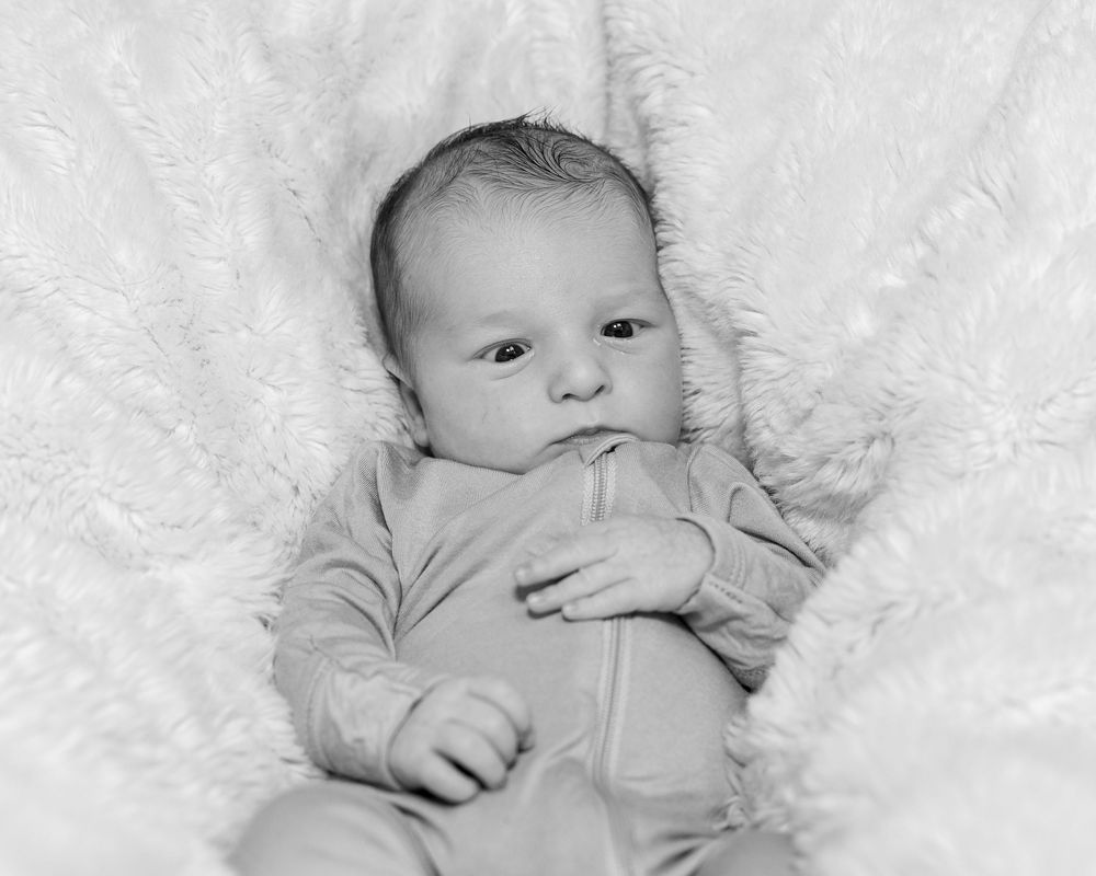 Infant in blue zippered sleeper on plush white blanket during a newborn portrait photo shoot in Sudbury, MA outside Boston, MA