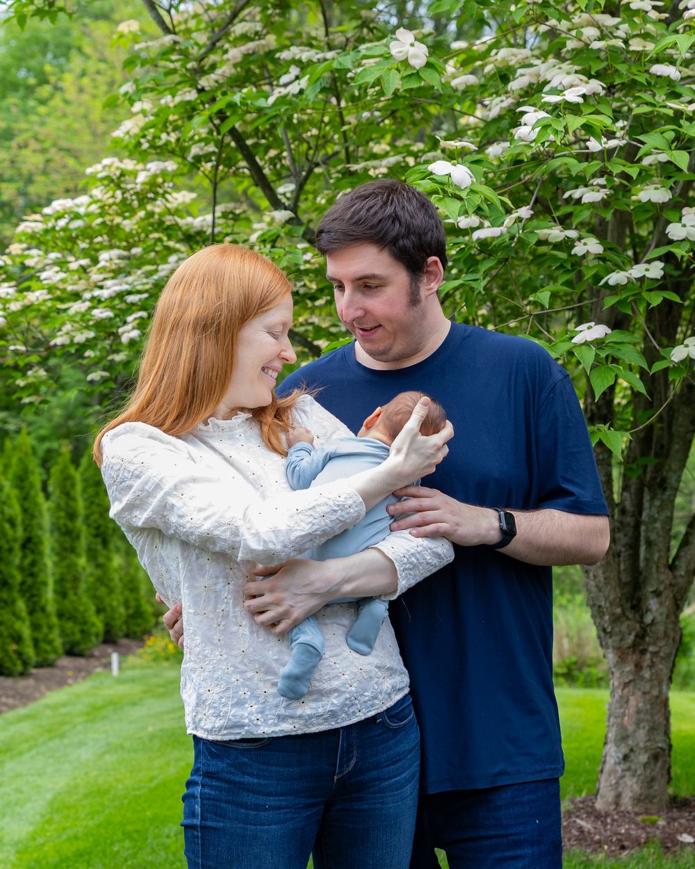Family shares tender moment under flowering tree in garden settingduring a newborn portrait photo shoot in Sudbury, MA outside Boston, MA