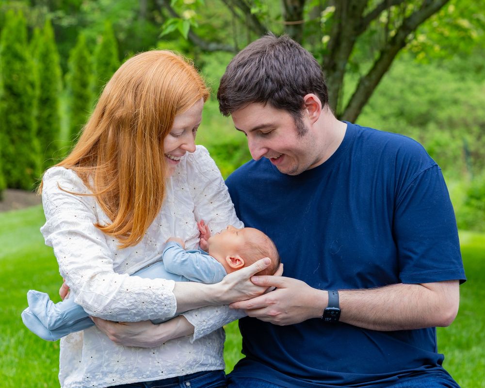 Parents gaze lovingly at their newborn baby while standing in a lush garden setting.