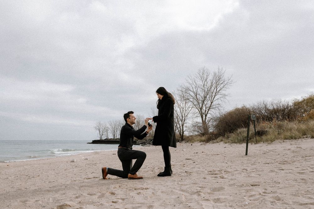 A romantic beach proposal moment silhouetted against a cloudy winter sky on a deserted shoreline.