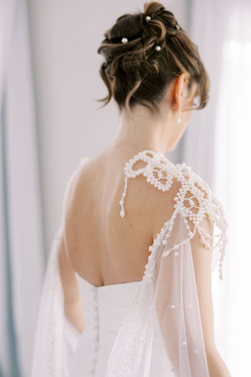 Back view of elegant bridal updo hairstyle with delicate beaded lace cape and open back wedding dress at Windham Manor.