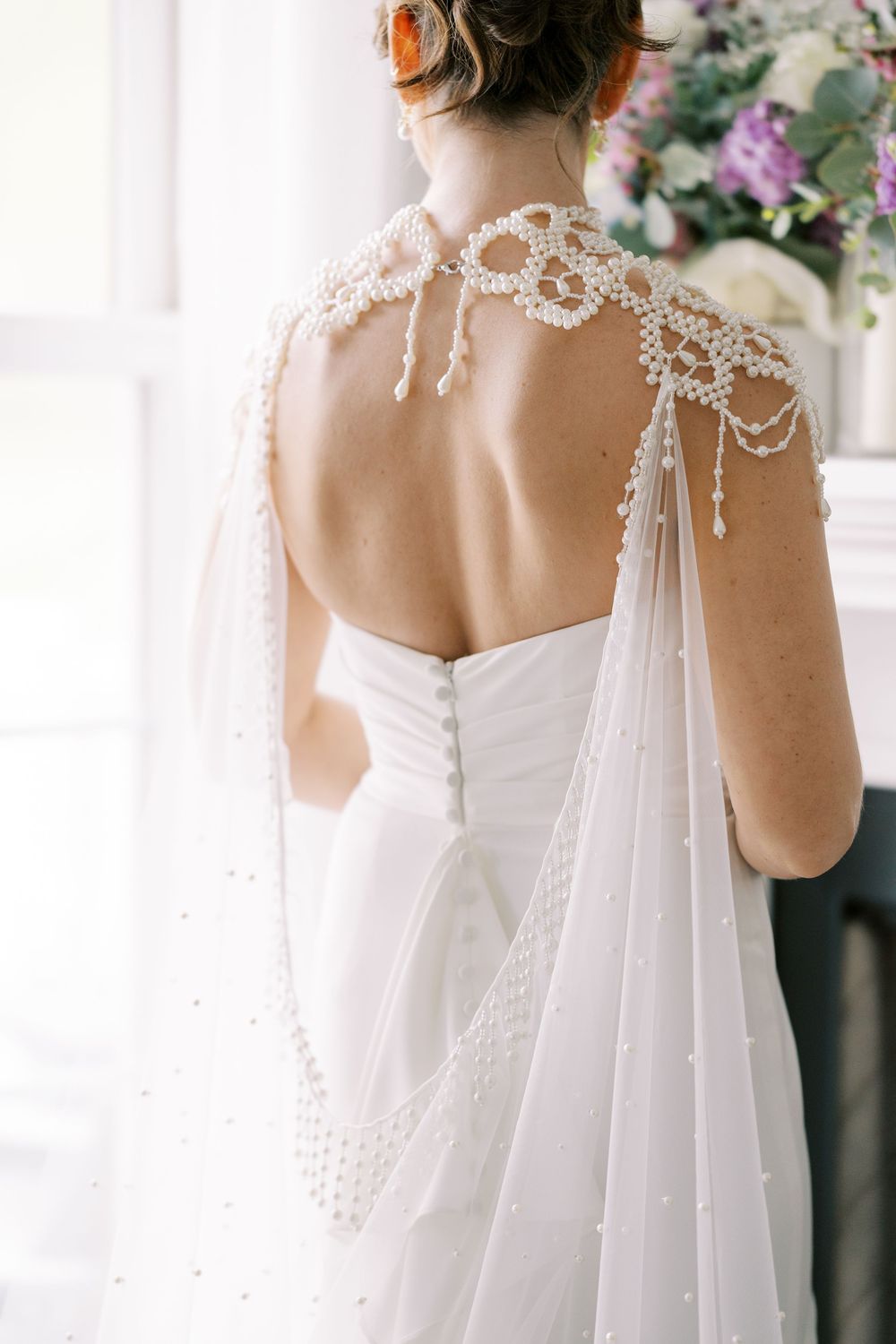 Elegant backless wedding dress with delicate pearl beaded cape and lace details shown from behind at Windham Manor.