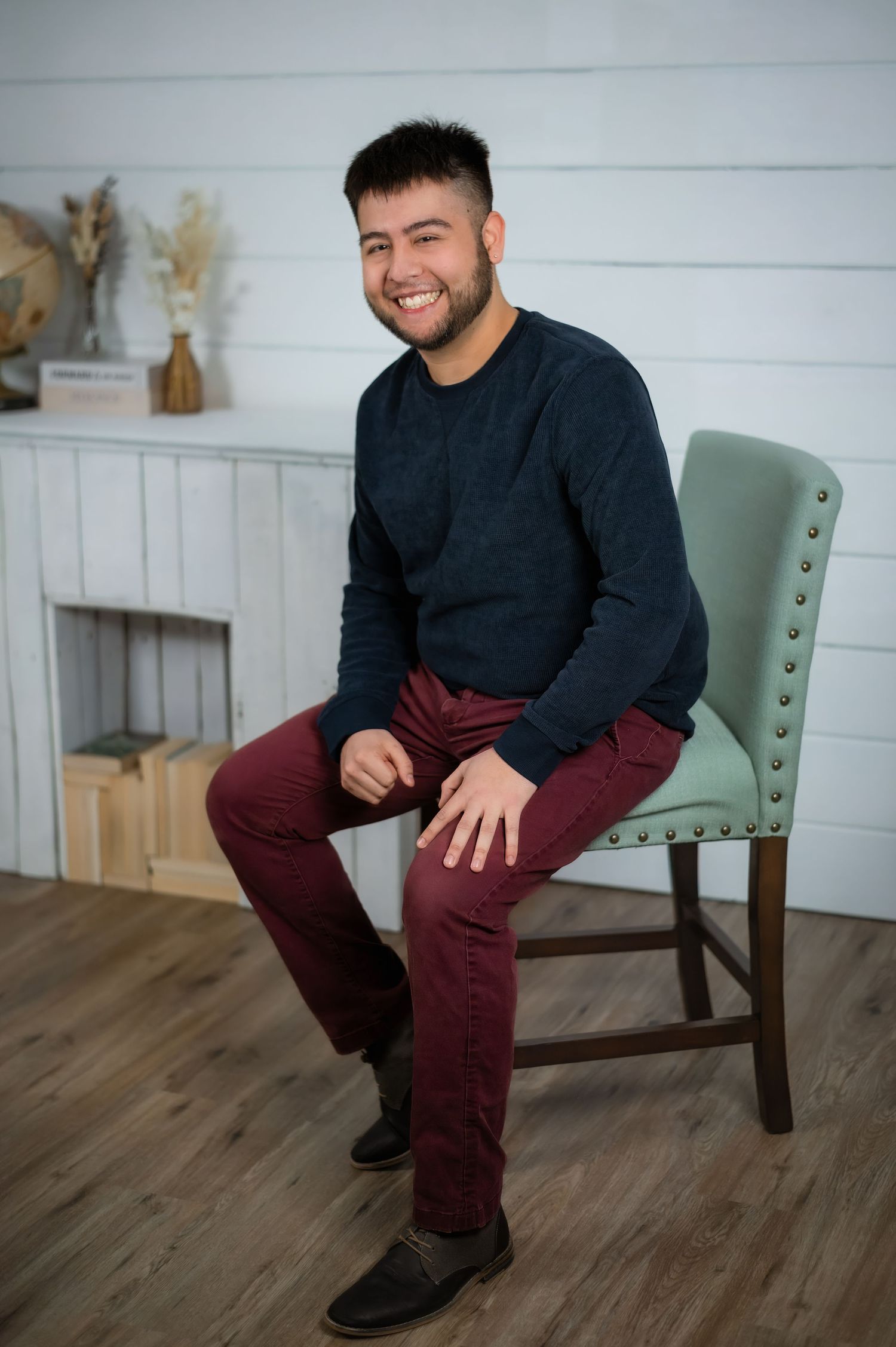Person wearing a black sweater and brown pants stands against white shiplap wall with vintage globe and wooden decor.