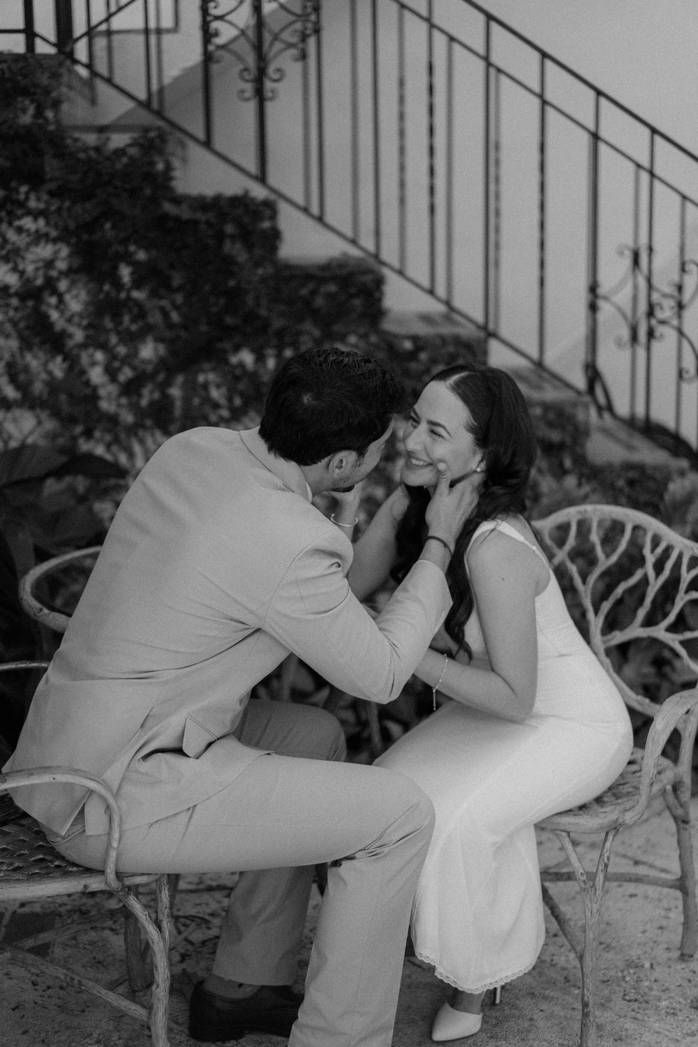Black and white romantic moment shared between couple sitting on outdoor patio furniture highlighting tender intimacy.