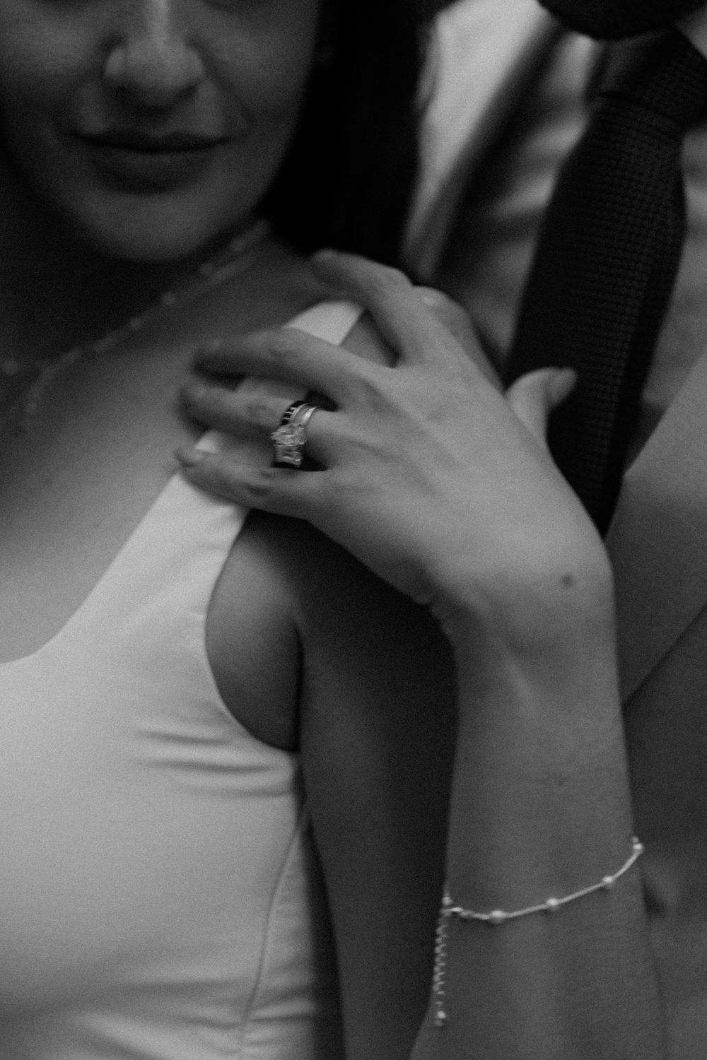 Close-up black and white photo showing a delicate engagement ring and bracelet on a person wearing white.