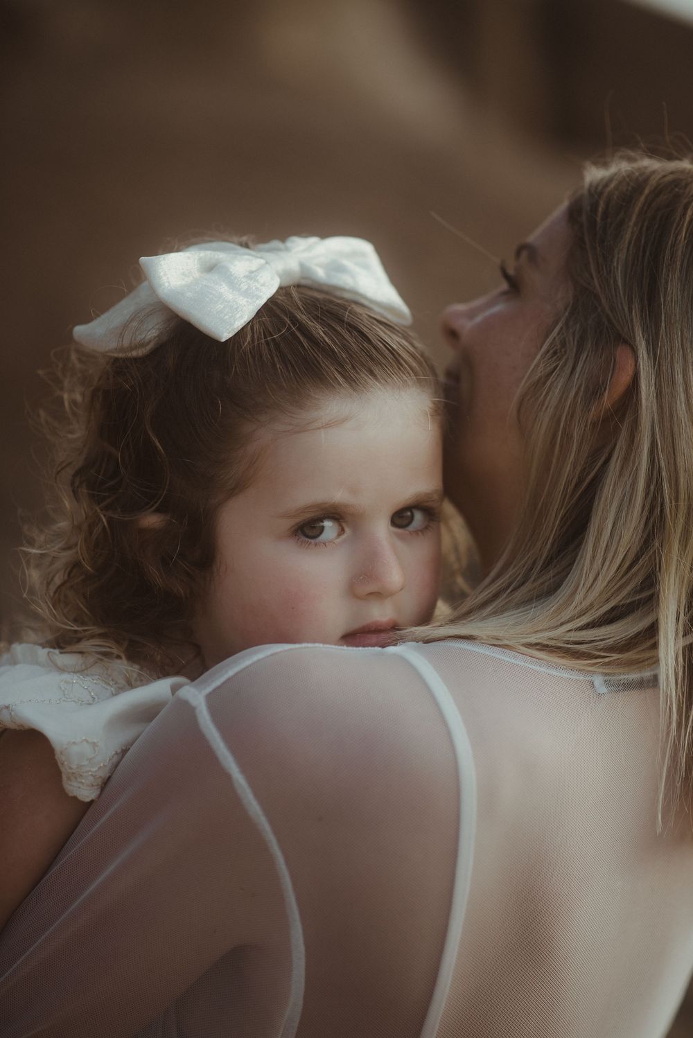 A tender moment captured between mother and child in soft sepia tones with a white hair bow.