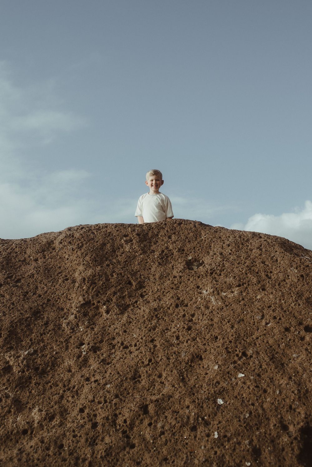 A small figure stands atop a large dirt mound against a cloudy sky backdrop.