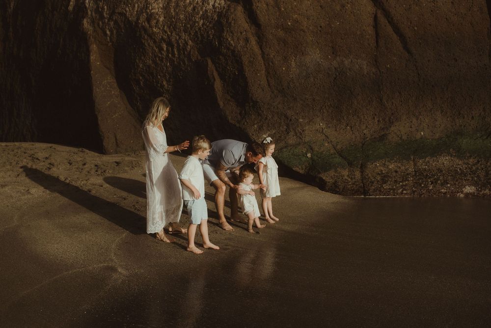 Four people in white linen clothing walk together in a dimly lit cave or cavern setting.