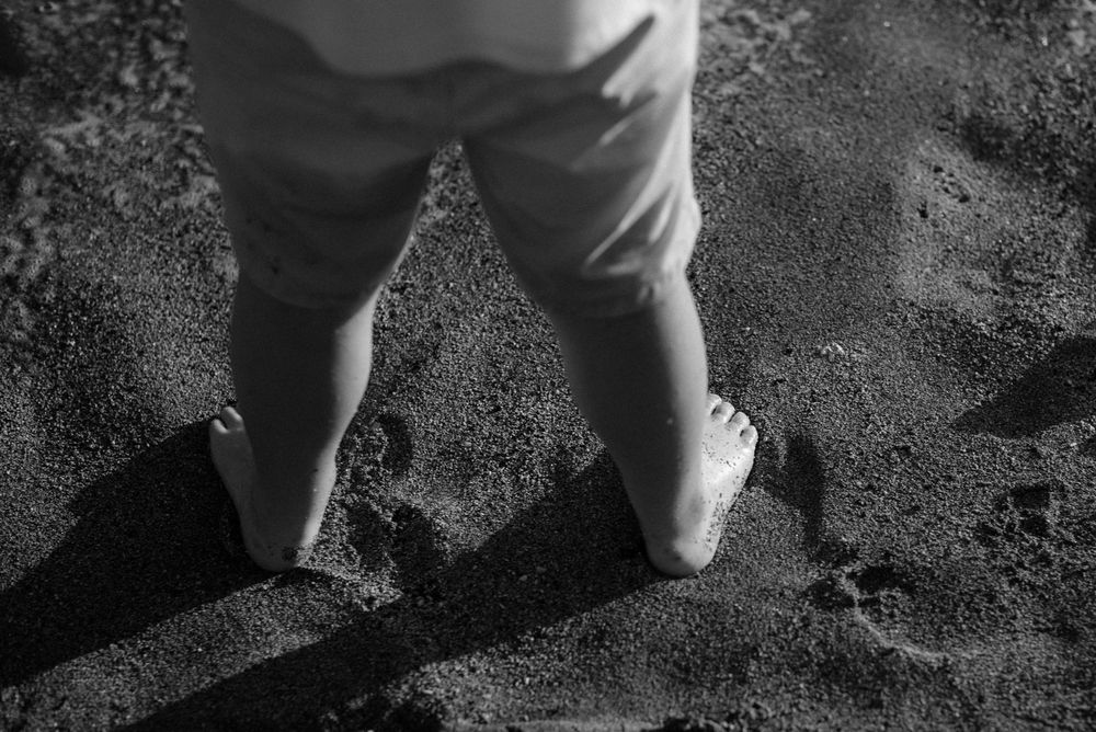 Black and white close-up of small feet and legs standing on dark ground casting shadows.