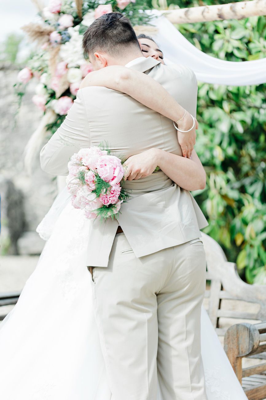 Photographe mariage Toulouse – étreinte des mariés à la cérémonie laïque, bouquet de pivoines en main et décor floral en extérieur