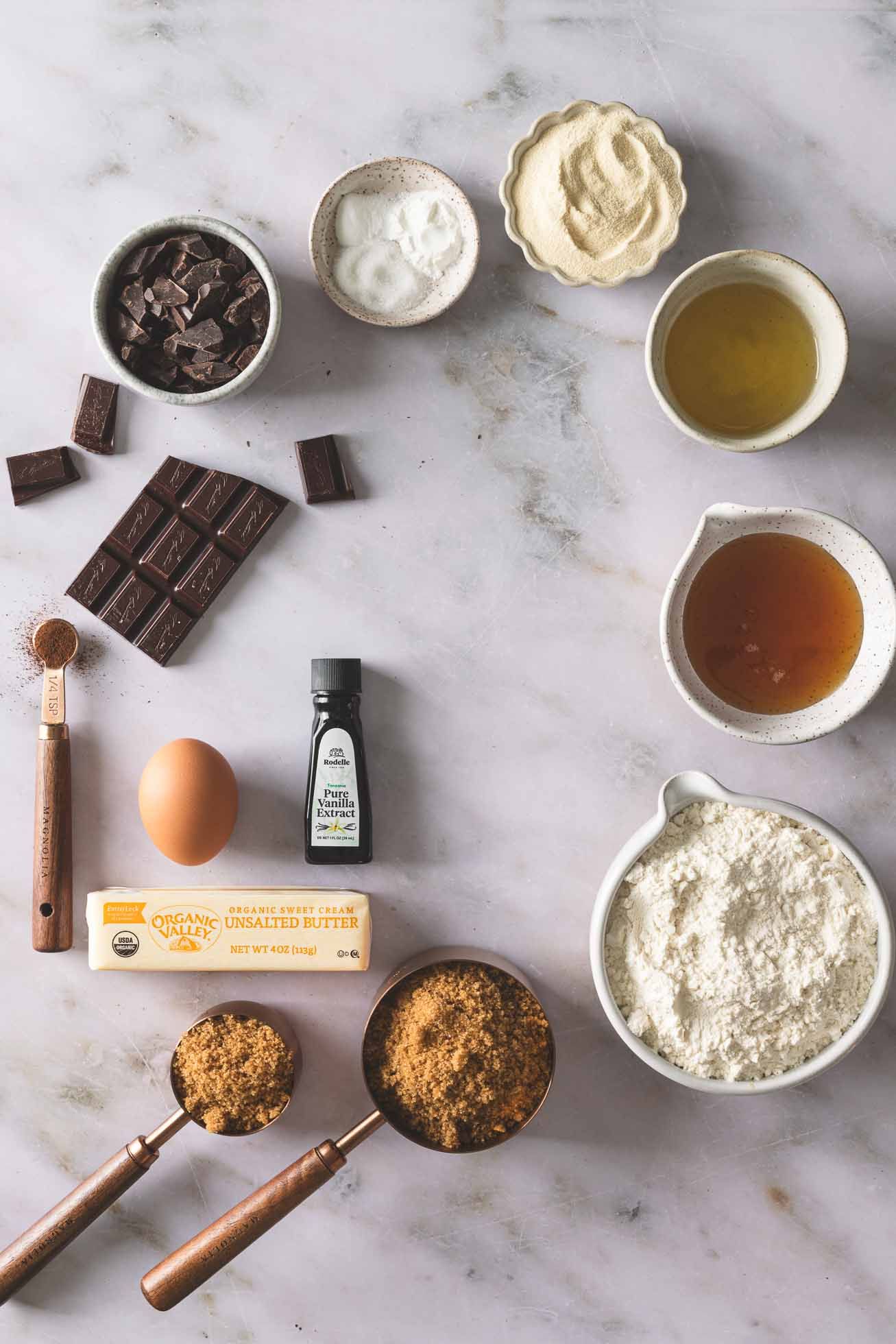 Baking ingredients including chocolate, butter, flour, sugar, and eggs arranged on a marble countertop for recipe preparation.