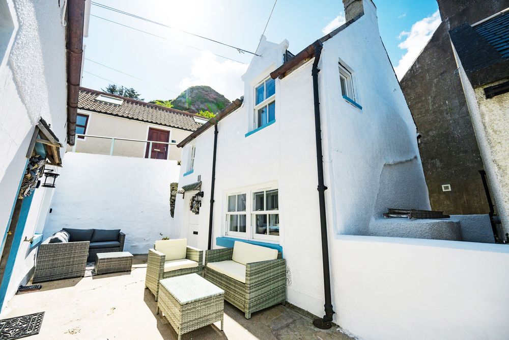 A white coastal cottage with outdoor patio furniture and blue trim features a cozy backyard seating area.