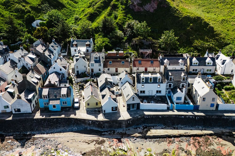 Aerial view of white coastal houses lined up along rocky shoreline in Scottish fishing village.