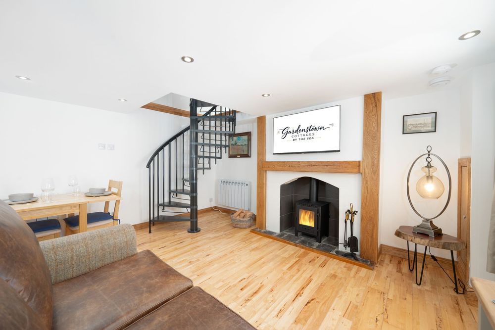 Living room with spiral staircase, wooden floors and black fireplace under white ceiling.