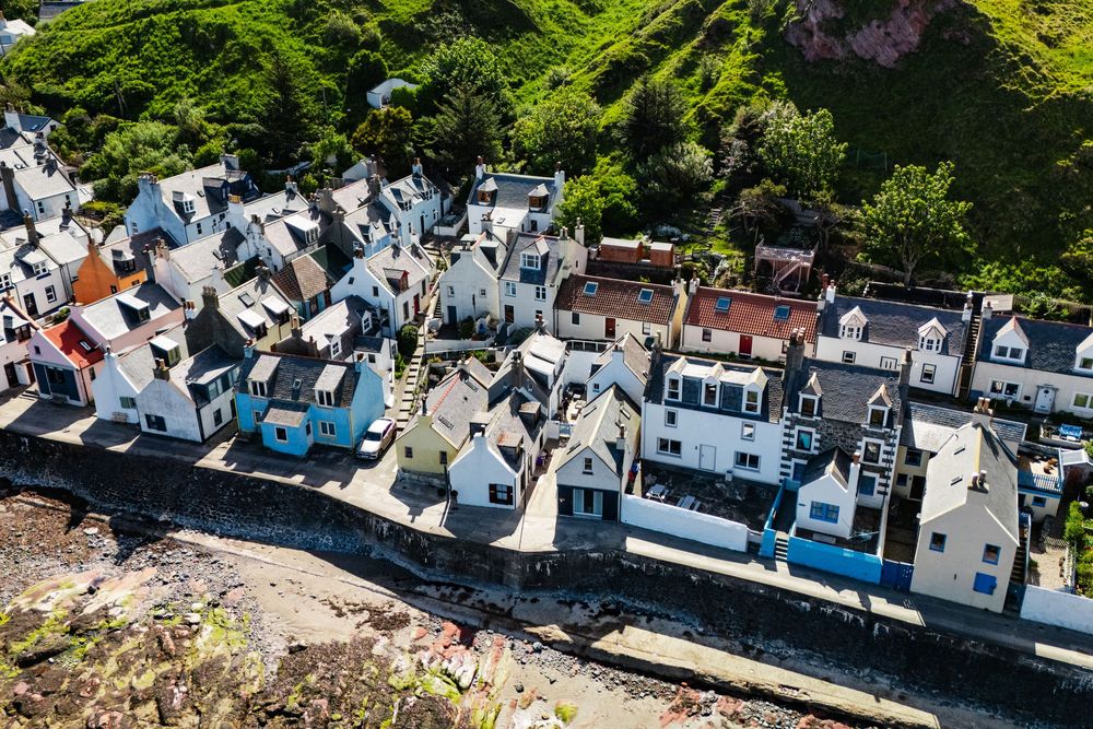 Aerial view of traditional white-painted houses lined up along a coastal street in a Scottish village.