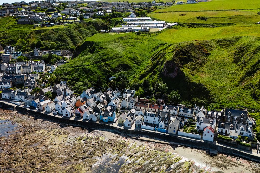 Scenic aerial view of white houses nestled along coastal cliffside with green hills in background.