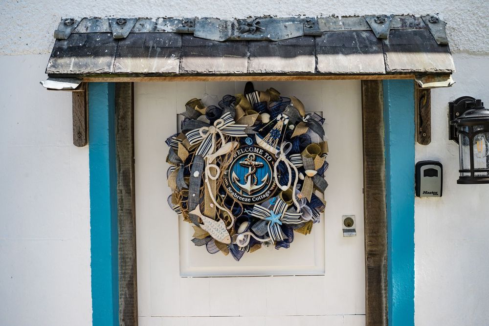 Decorative wreath made of driftwood and nautical elements mounted on white door with turquoise trim.