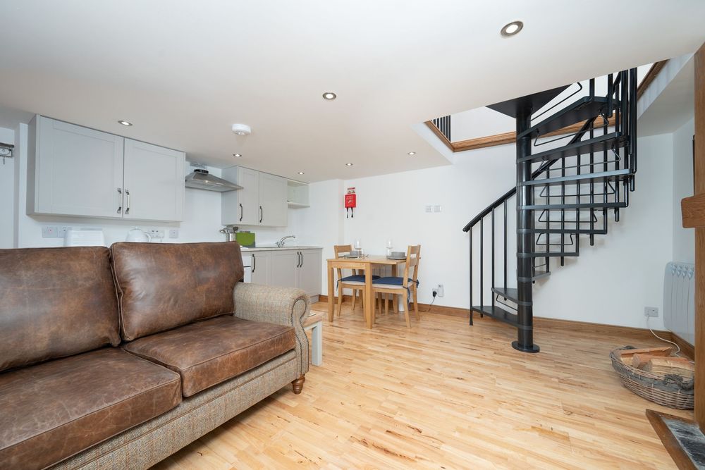 Modern open plan living space with brown leather sofa, spiral staircase, and light wood flooring in a duplex apartment.
