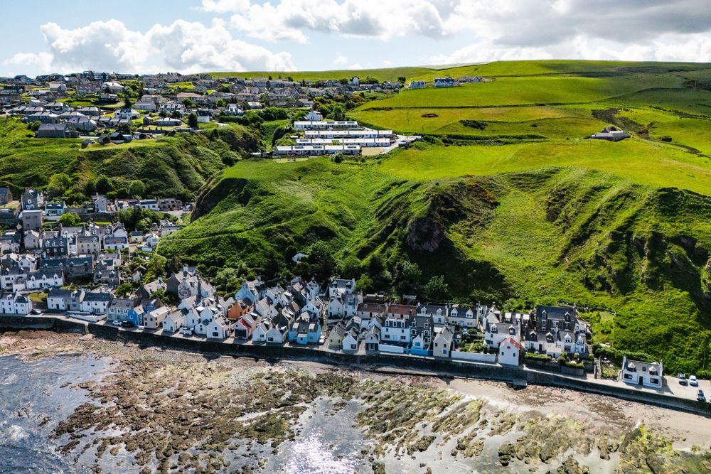 Aerial view of a coastal village nestled on green cliffs with white buildings along the shoreline.