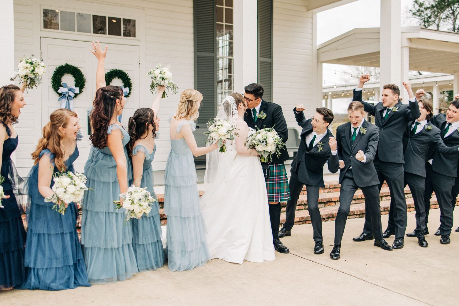 Wedding party dressed in blue and black poses in an elegant outdoor venue during a celebration.