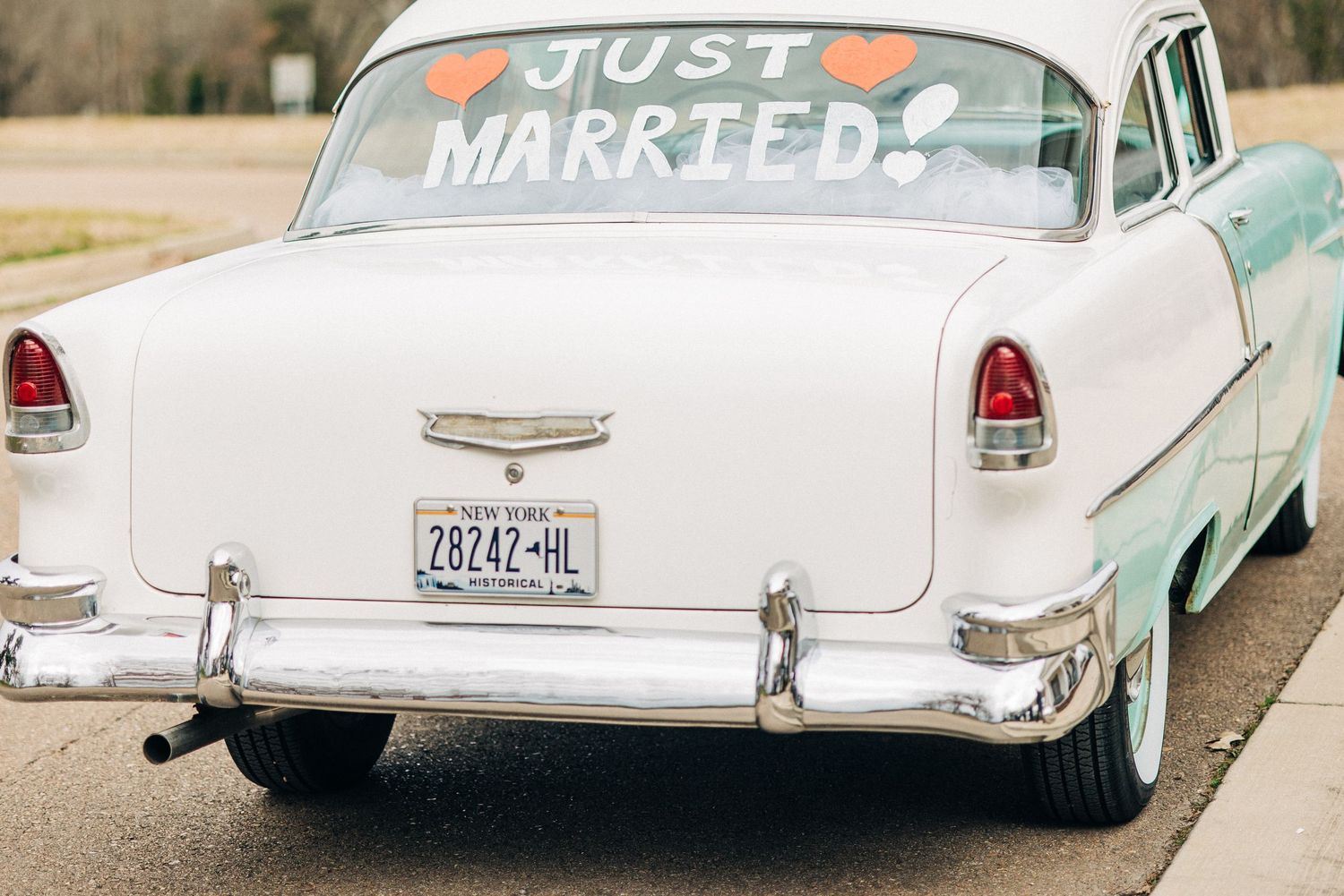 White vintage wedding car decorated with Just Married text and hearts displays retro elegance.