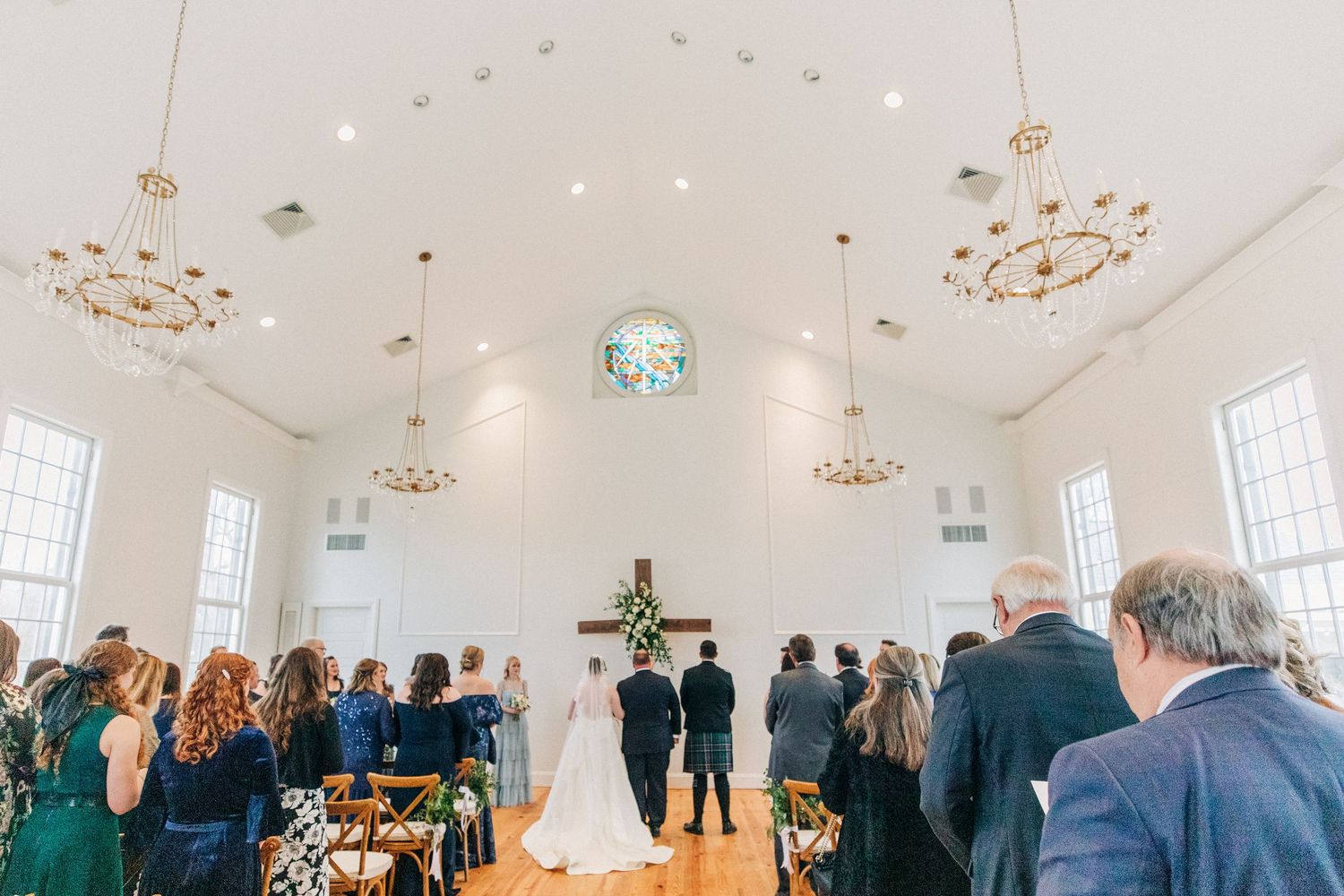 Bride and groom celebrate during a grand wedding reception in an elegant white ballroom with crystal chandeliers.