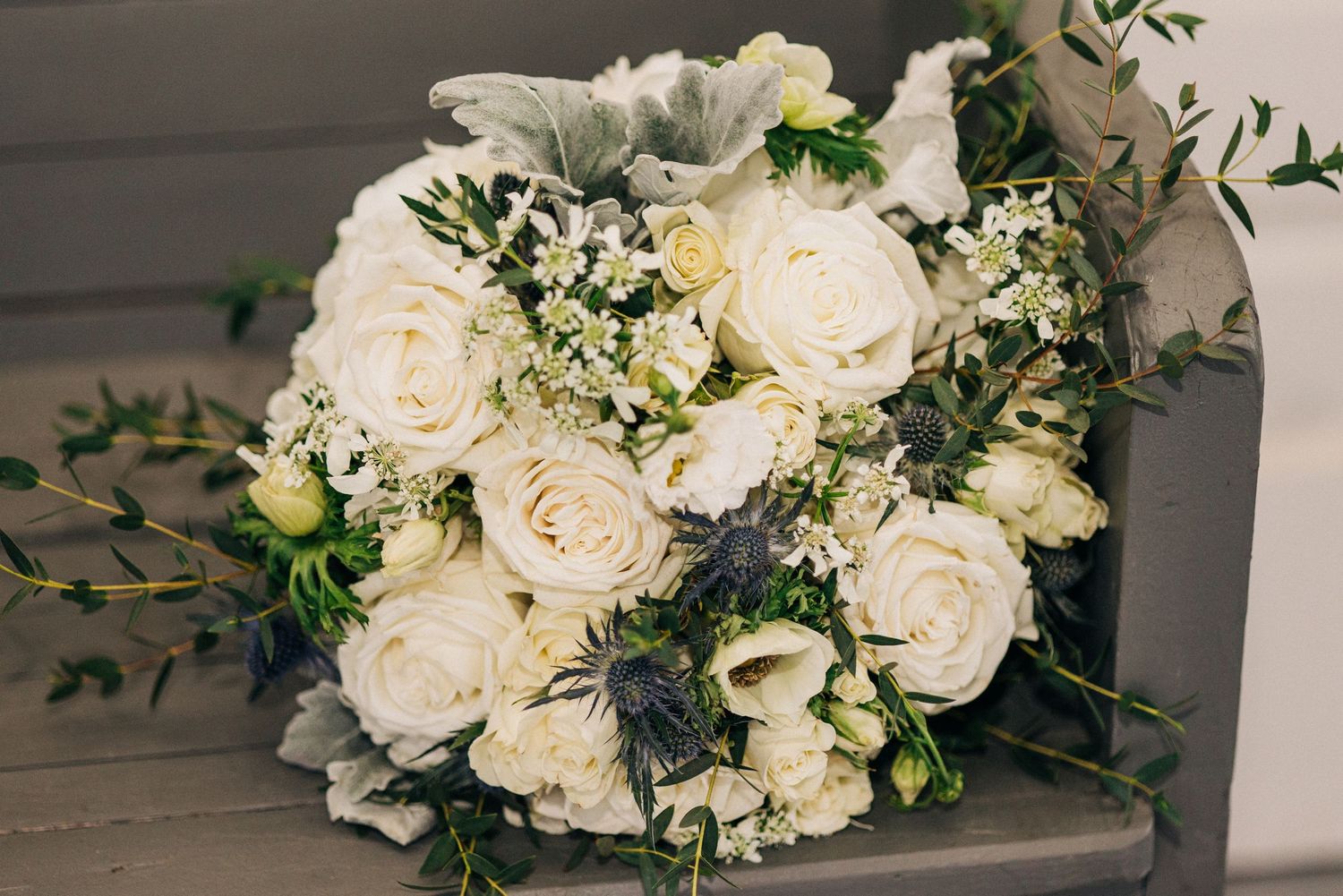 Beautiful white garden roses and eucalyptus wedding bouquet arranged in classic style against a neutral gray background.