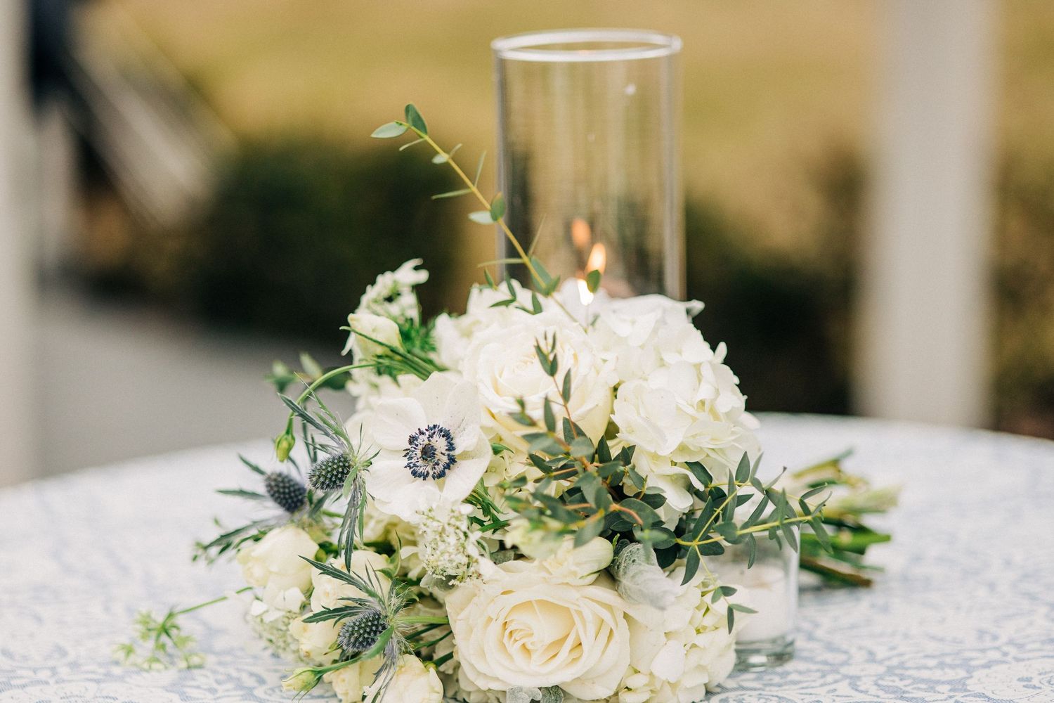 Elegant white floral centerpiece with delicate roses and greenery arranged on white linen tablecloth at wedding reception.