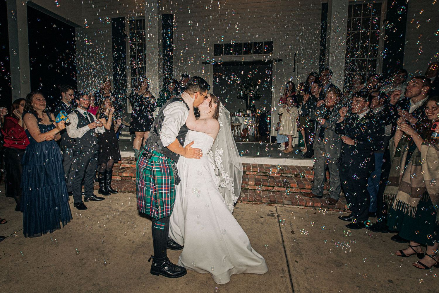 A couple shares their first dance at their wedding while guests throw confetti in a rustic indoor venue.