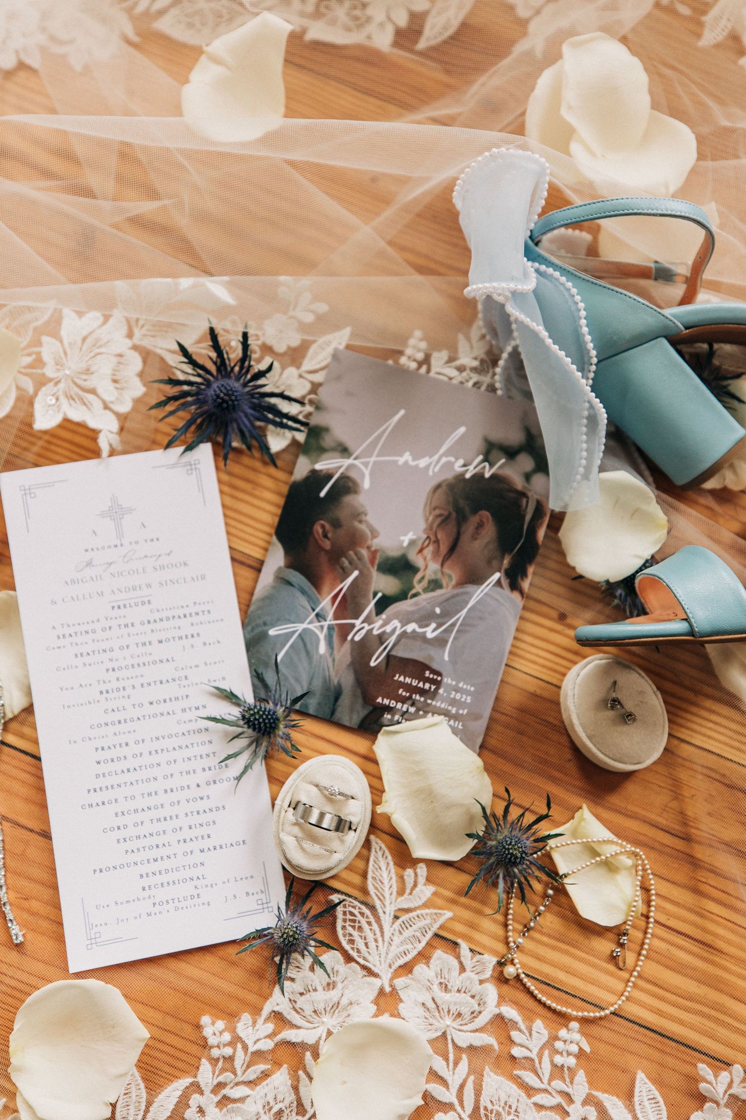 Wedding details flat lay with invitation, teal shoes, dried flowers and decorative elements on wooden surface.