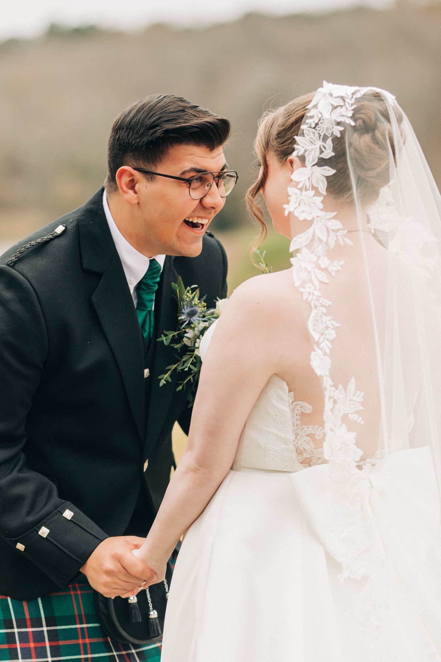 A joyful wedding moment captured between newlyweds with the groom wearing a traditional Scottish kilt and emerald tie.