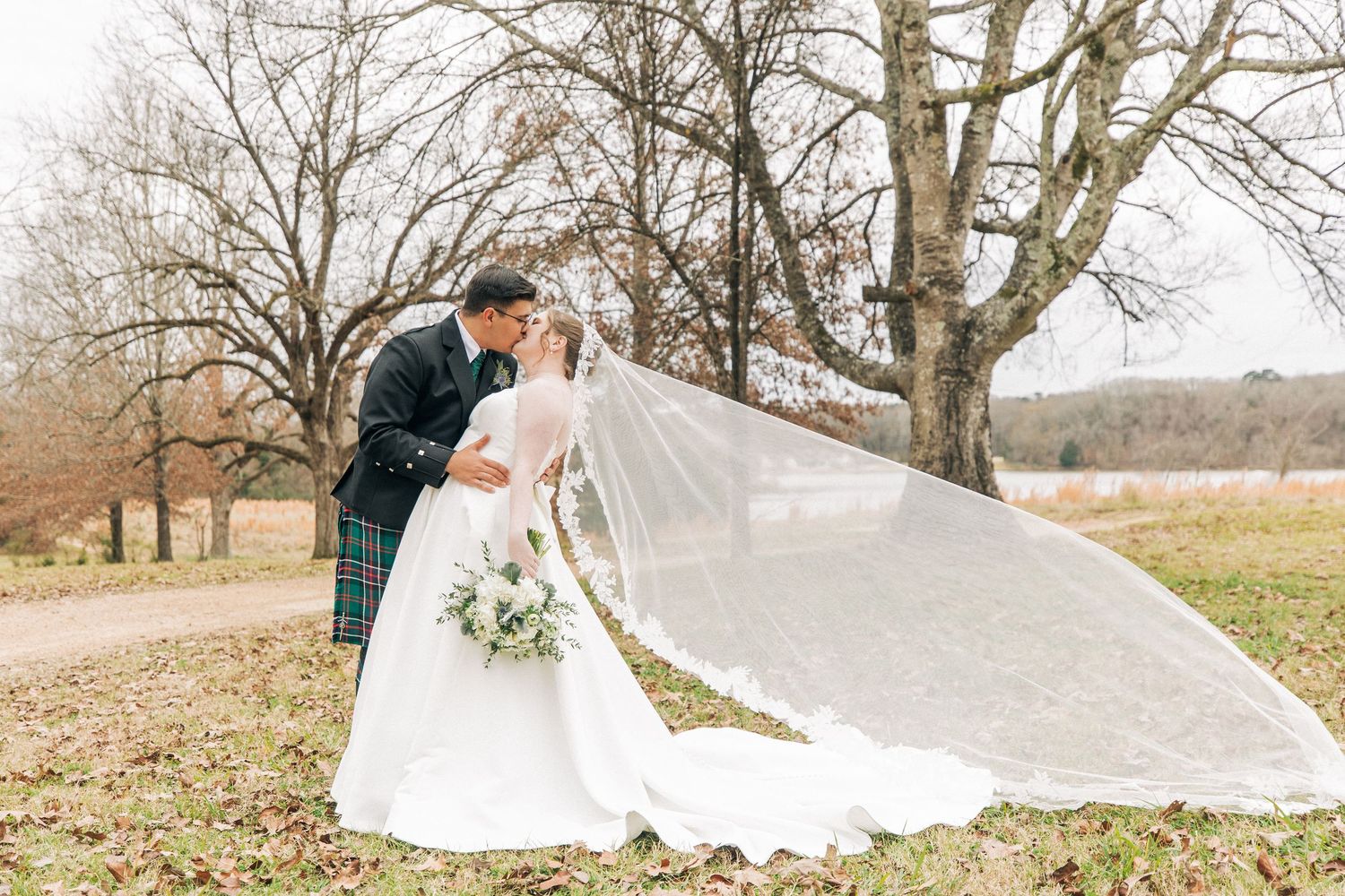 A couple in formal attire embraces in multiple romantic poses along a scenic pathway surrounded by autumn trees.