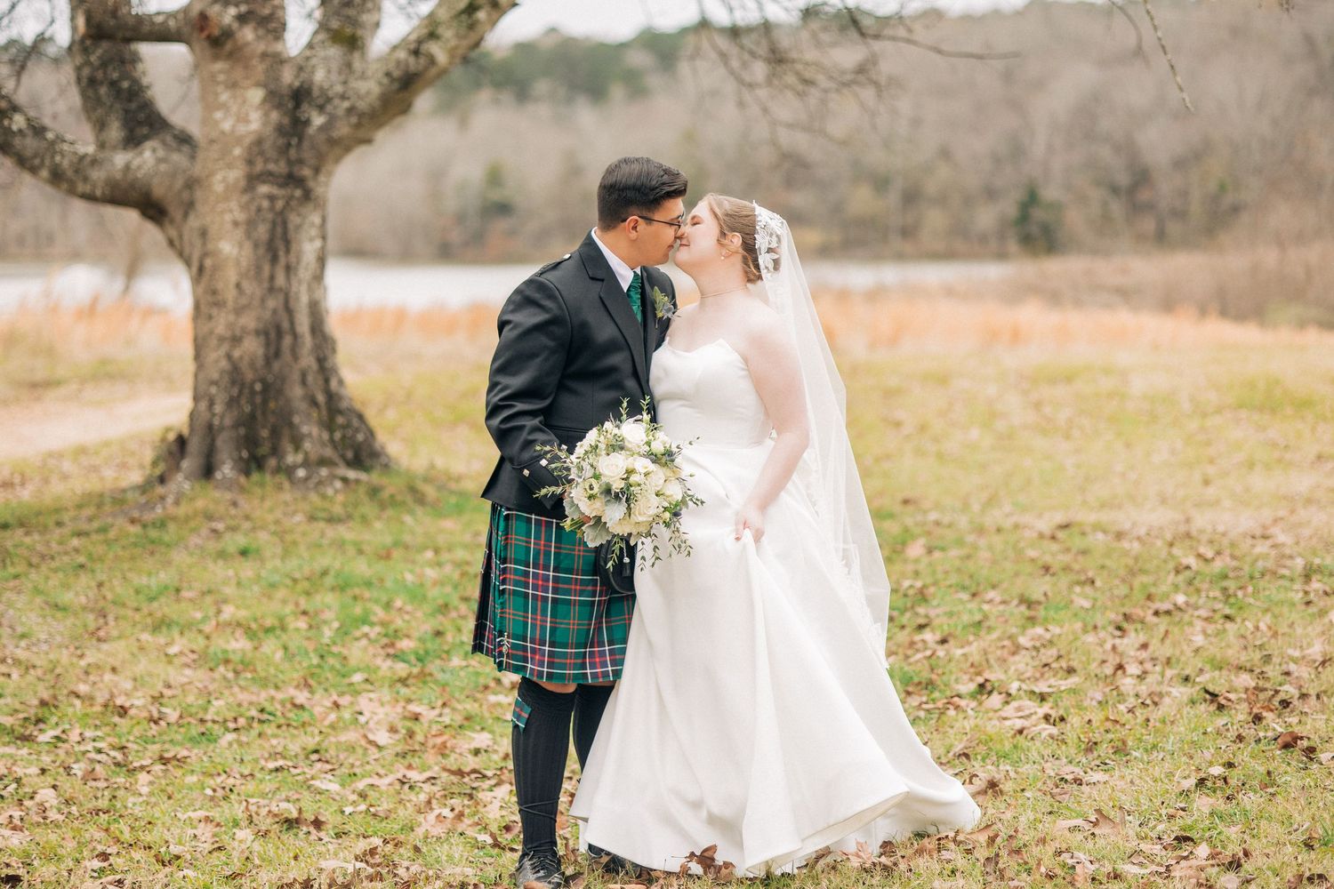 A romantic wedding couple embraces on a meadow in autumn with the groom wearing a traditional Scottish kilt.