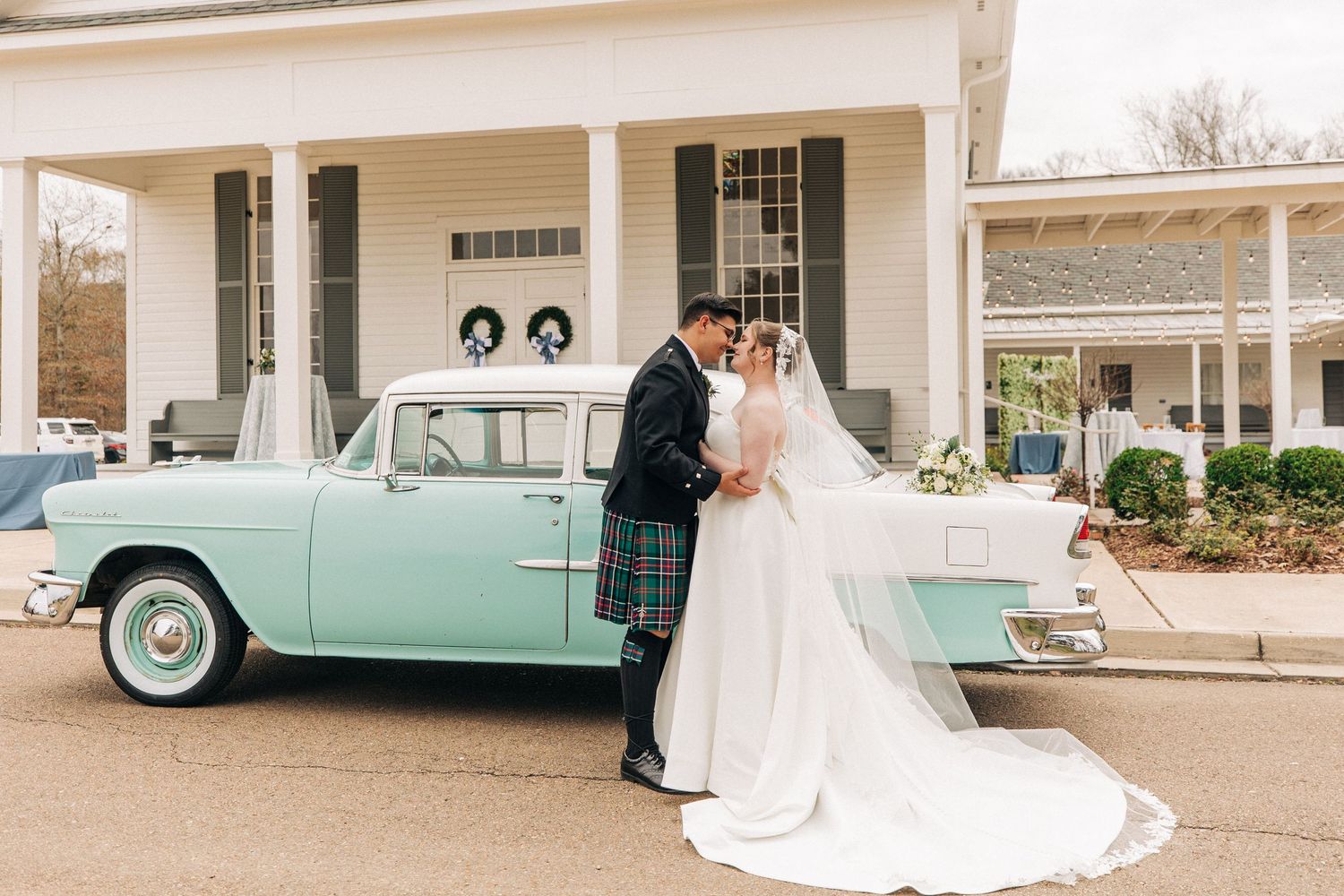 A vintage mint green classic car serves as a backdrop for romantic wedding photos in front of a white building.
