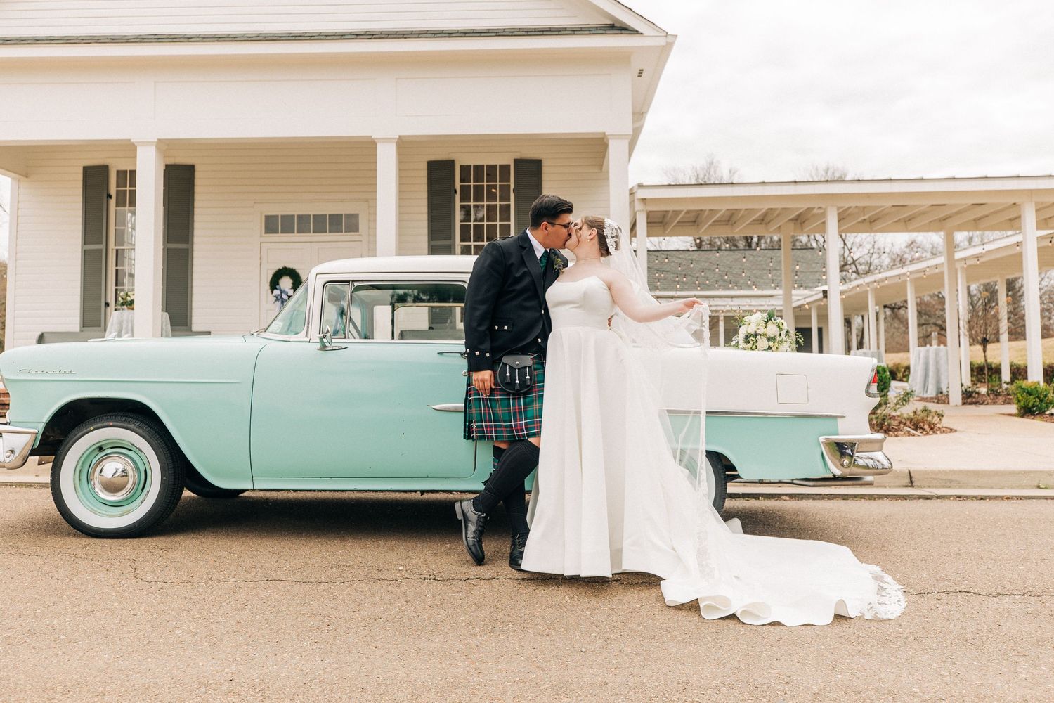 A vintage mint green Chevrolet parked in front of a white columned building serves as backdrop for a couple in wedding attire.