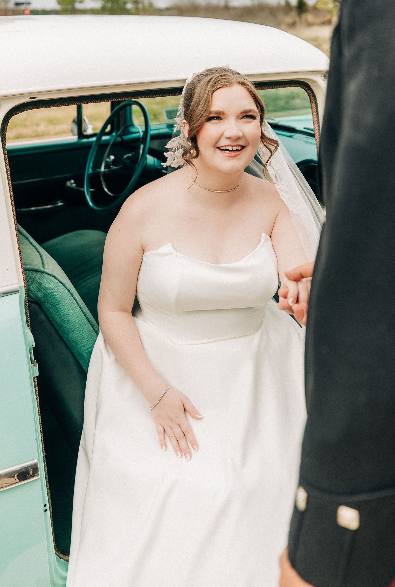 Bride in a classic white wedding gown stands beside a mint green vintage car on her wedding day.