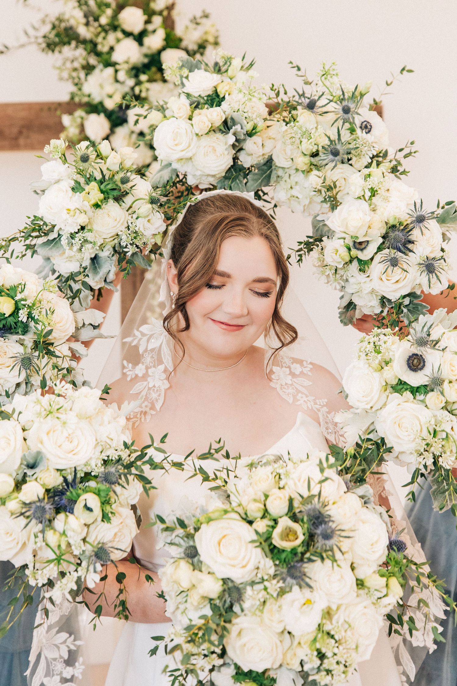 A romantic wedding portrait featuring white roses and greenery arranged in a circular floral arch with delicate veil details.