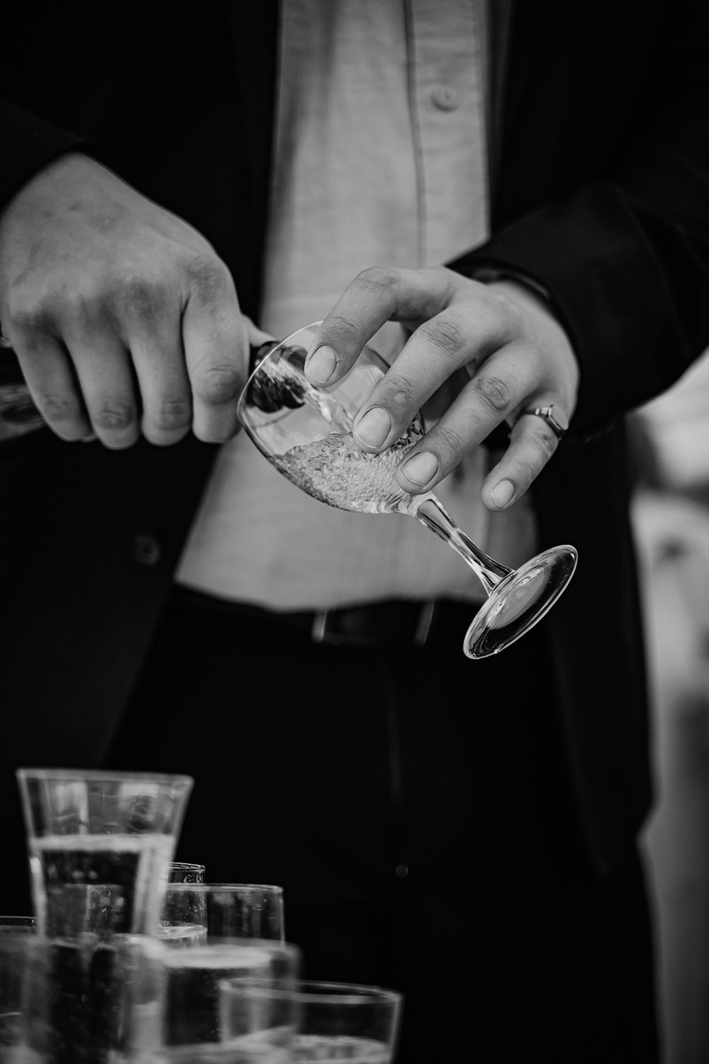 En man häller upp vin i ett glas under mingel på bröllop i trädgården vid Borkhult Lapphult, bröllopsfotograf Josefin Landhagen i Åtvidaberg