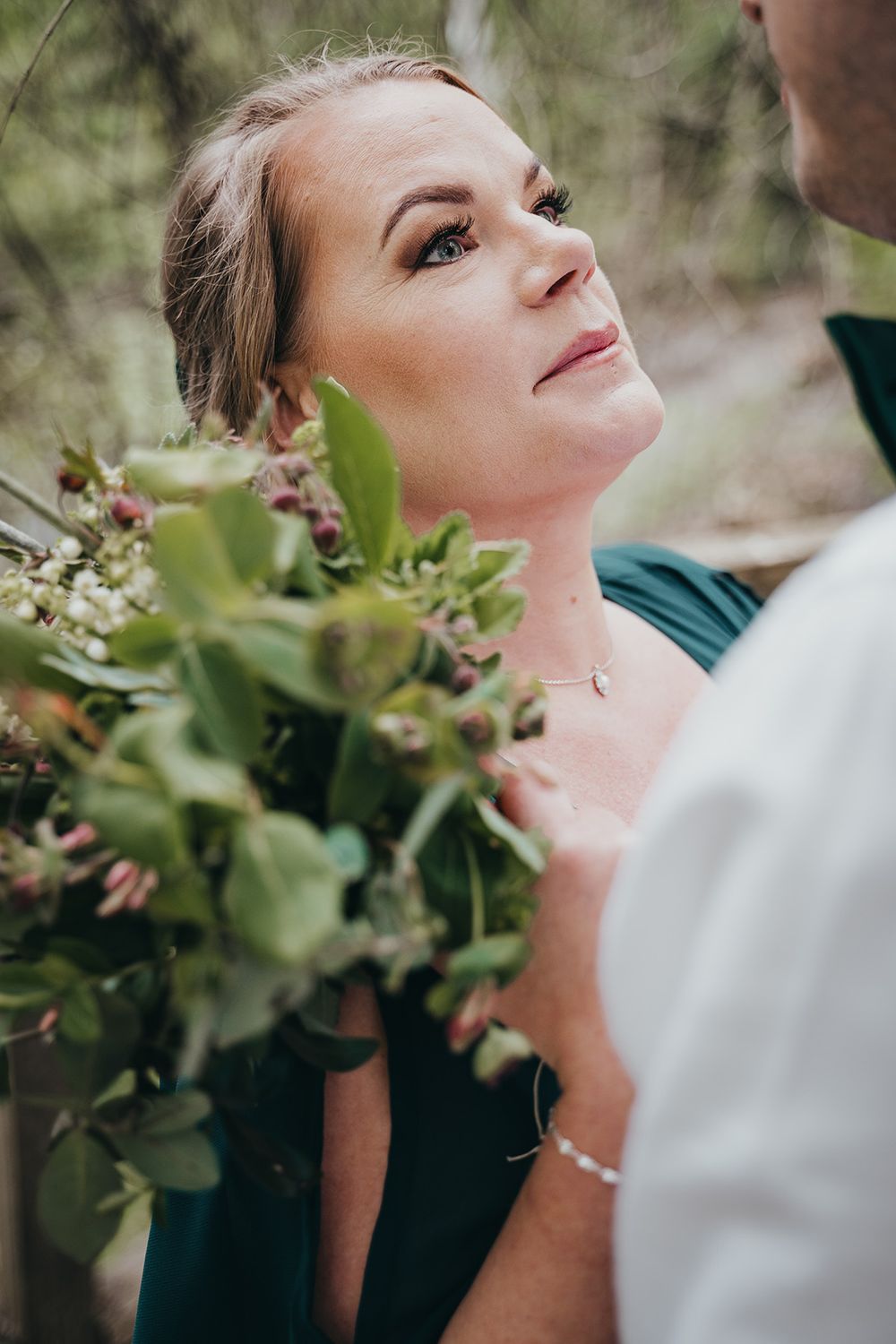 Porträtt på brud iklädd en grön brudklänning. Hon håller i en brudbukett med vårblommor av liljekonvalj och gullvivor.